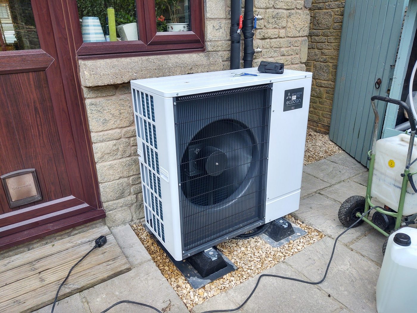 A Mitsubishi Ecodan outdoor unit set on gravel against a stone wall on a recent job near Cinderford