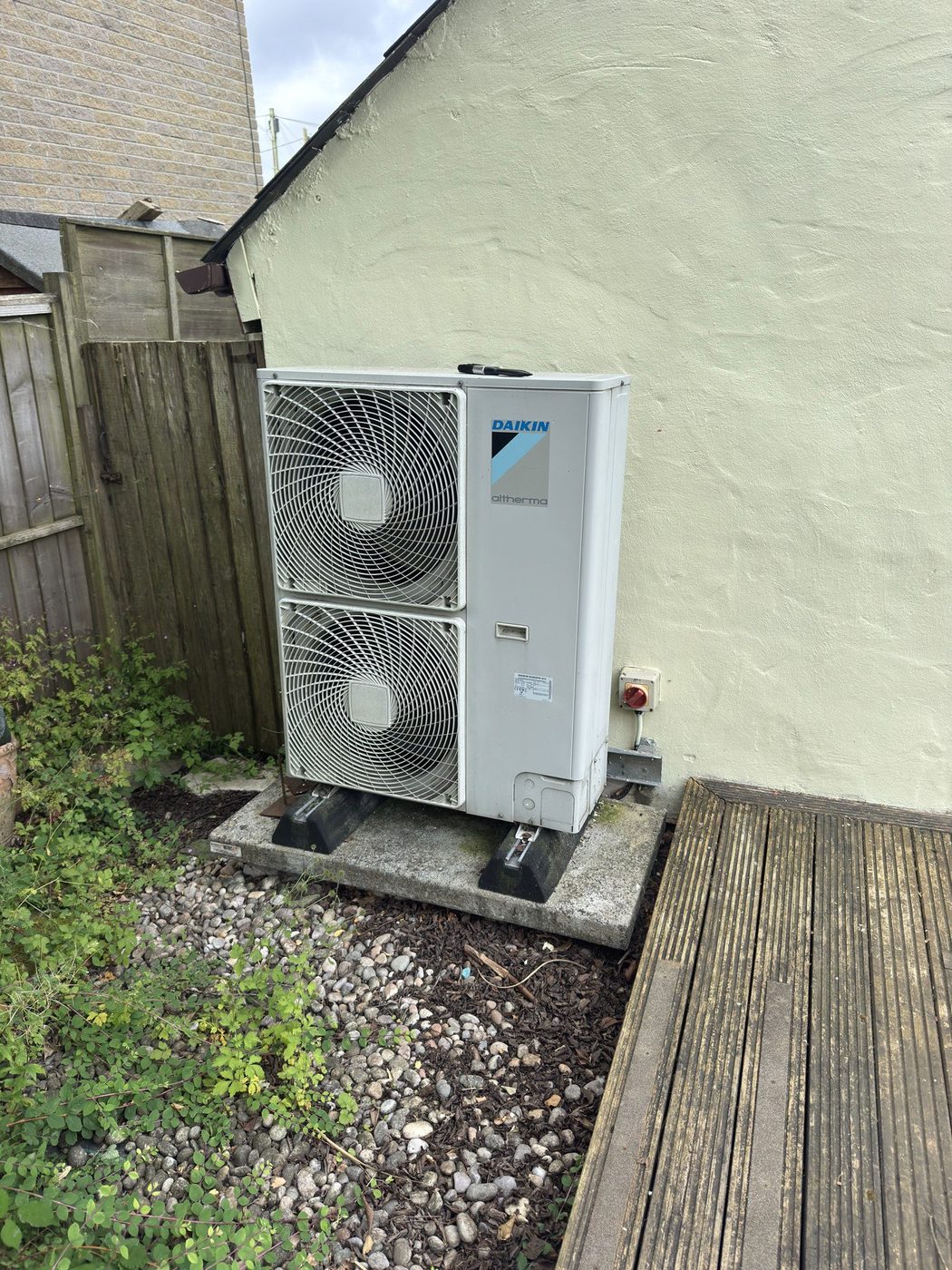 An older twin-fan Daikin Altherma heat pump on a plinth beside garden decking, serviced during a visit