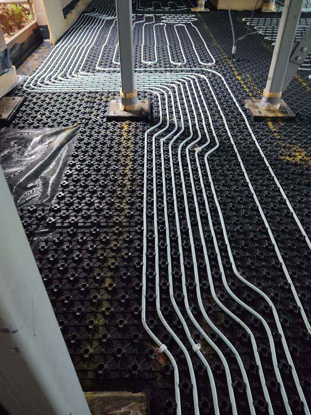 Underfloor heating pipe circuits clipped into black castellated panels before screeding