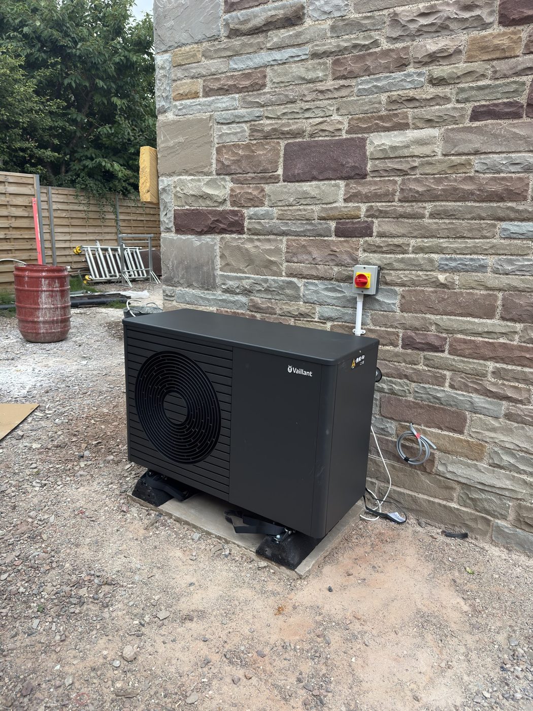 An anthracite-coloured Vaillant outdoor heat pump unit against a stone wall
