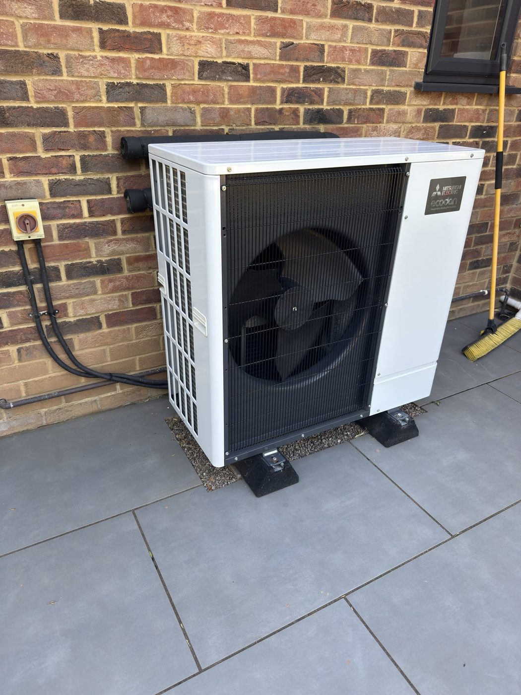A Mitsubishi Ecodan outdoor unit sited on a patio against a brick wall