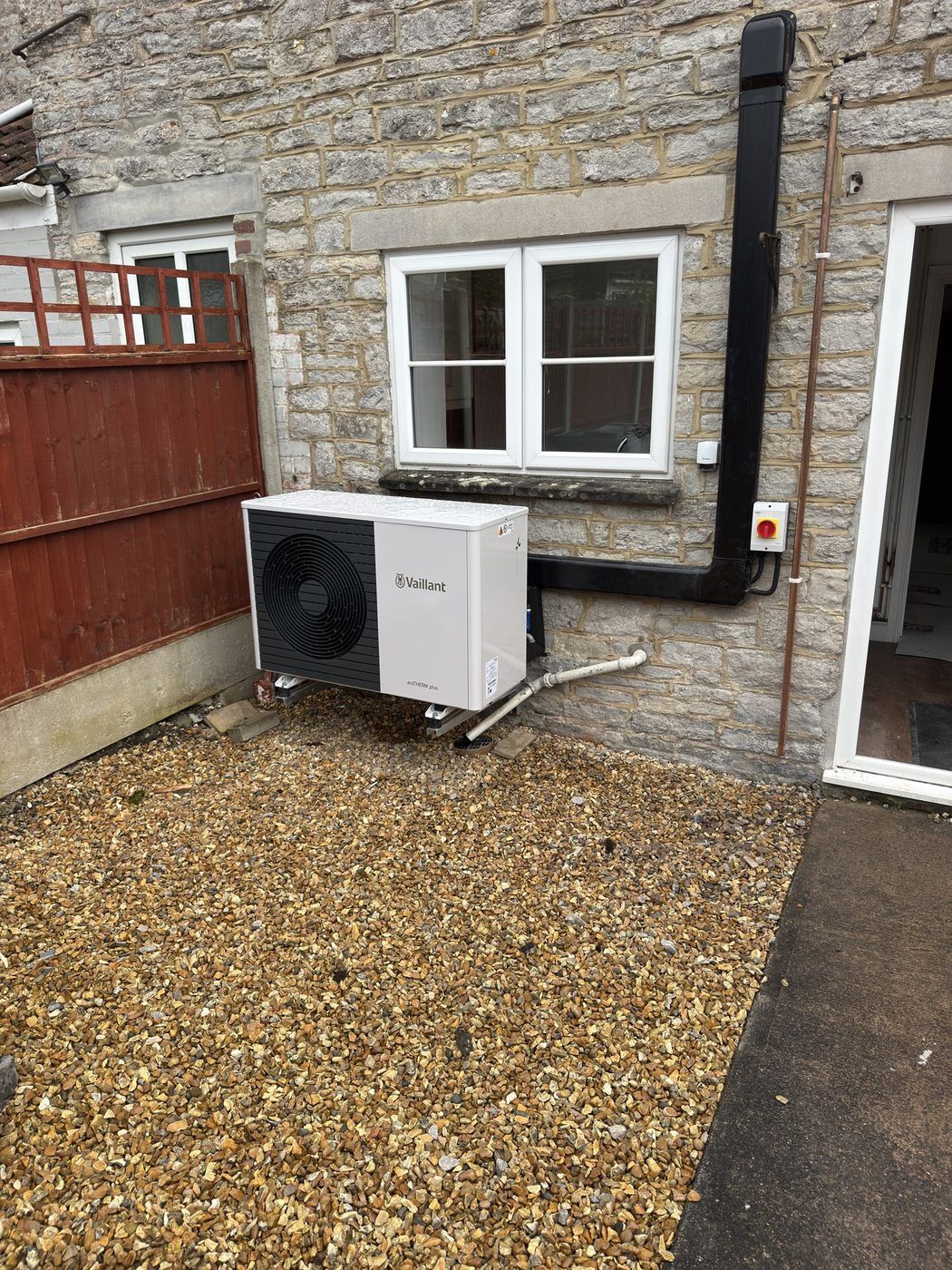 A Vaillant outdoor heat pump unit sited against a stone wall on a gravel bed