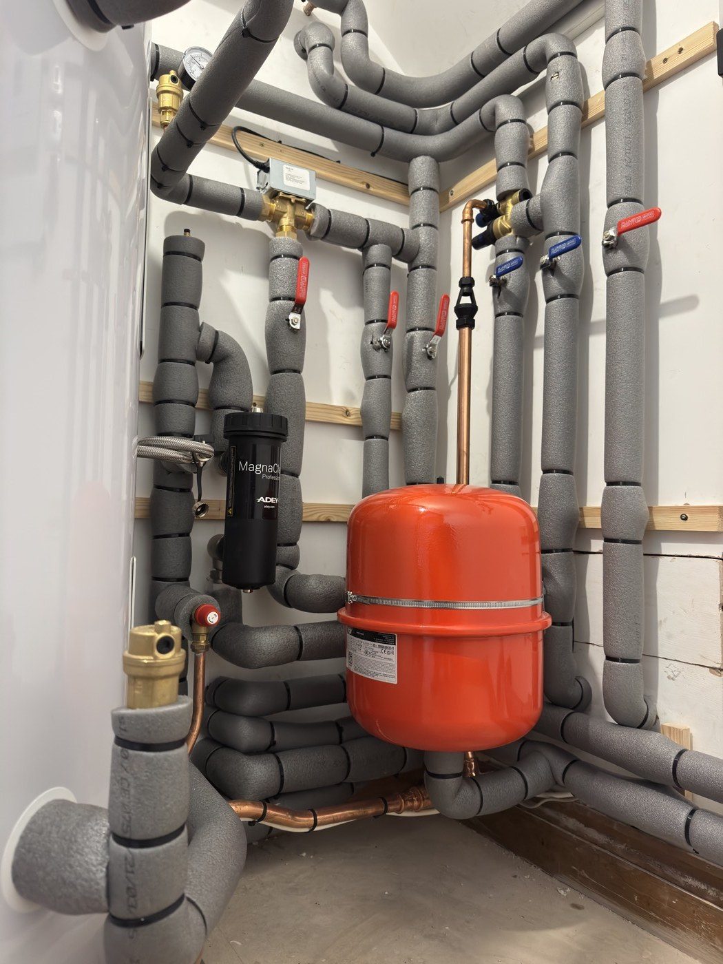 A neatly insulated plant wall with magnetic filter, expansion vessel and lagged pipework