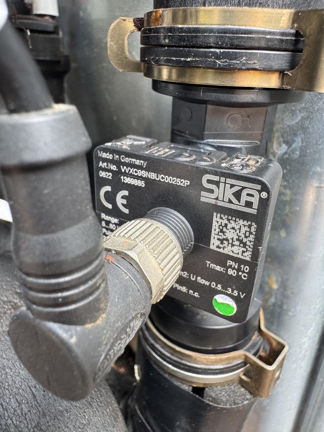 Flow sensor in place on the pipework, showing the part number and flow direction marking