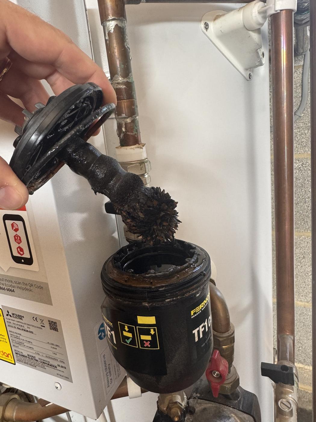 Magnetic filter magnet lifted out, thick with black iron sludge, before cleaning