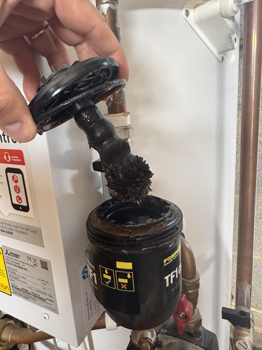 A magnetic filter lifted out on a service, its magnet coated in black iron sludge from the system water